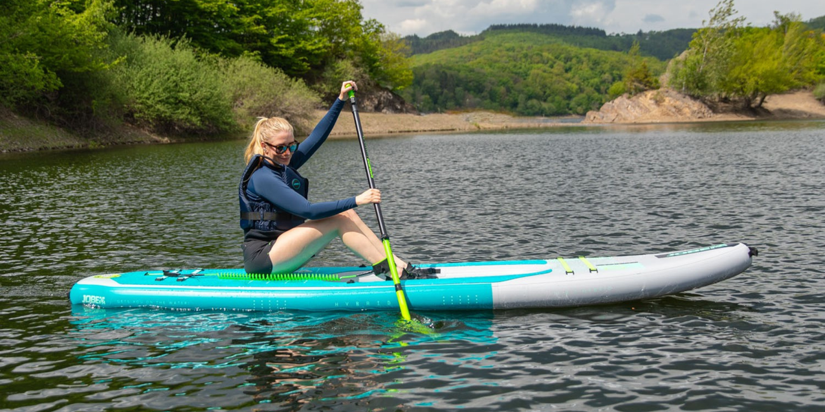 A woman sitting on a turquoise paddleboard